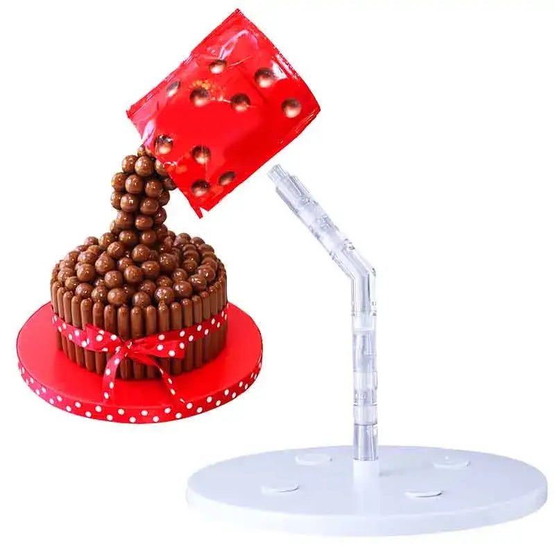 A red glossy cup pours chocolate maltesers onto a kitkat cake on a gravity defying white cake stand support structure