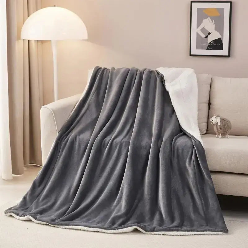 A plush gray and white reversible sherpa twin blanket draped over a sofa for cozy bedroom use
