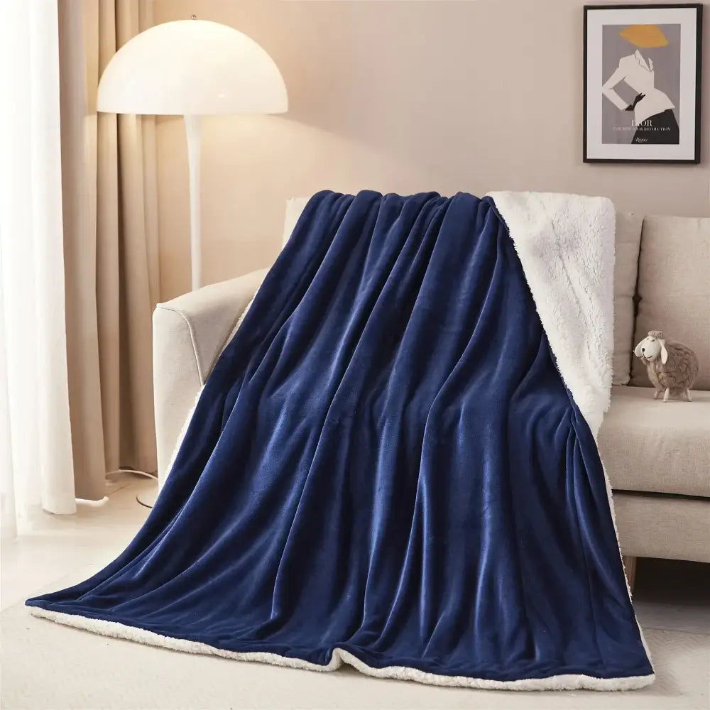 A plush navy blue and white sherpa twin blanket reversible throw draped over a sofa for bedroom use