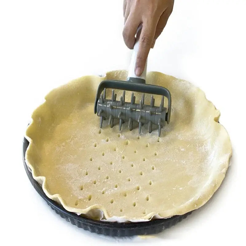 Gray and white silicone pastry wheel decorbites dough roller used on pale yellow dough in black tart pan