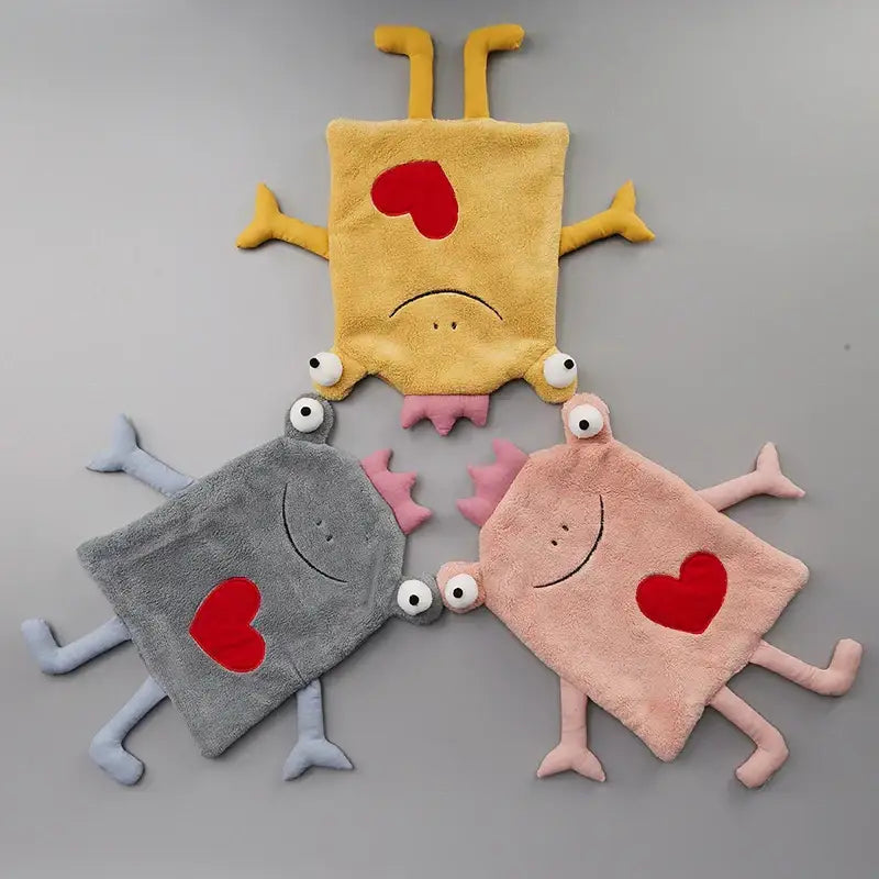Three plush soft-bodied monster baby blankets in yellow gray and pink with red hearts featuring decorbites frog design hand towel