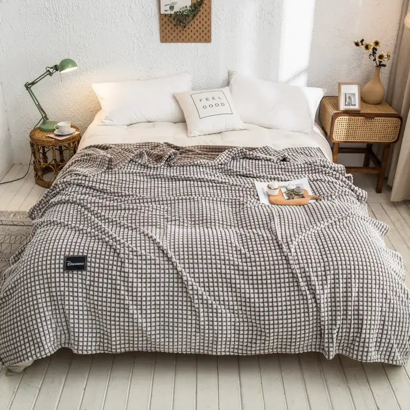 A cozy gray plaid coral fleece bed blanket with a soft checkered weave draped over a bedroom bedspread