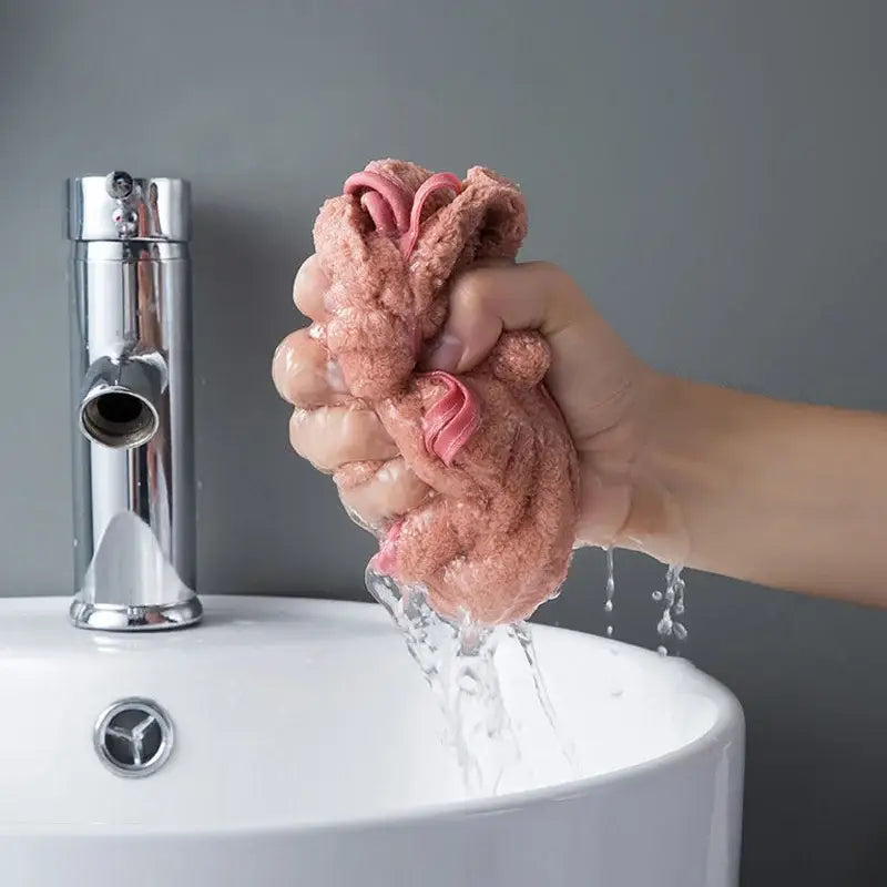 A soft pink bowknot coral velvet hand towel being squeezed to drain water in kitchen cleaning use by decorbites