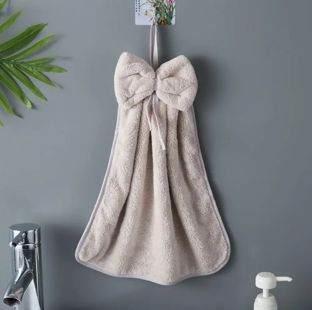 A beige plush hand towel with a large bowknot coral velvet bow hangs from a hook for kitchen cleaning decorbites bowknot coral