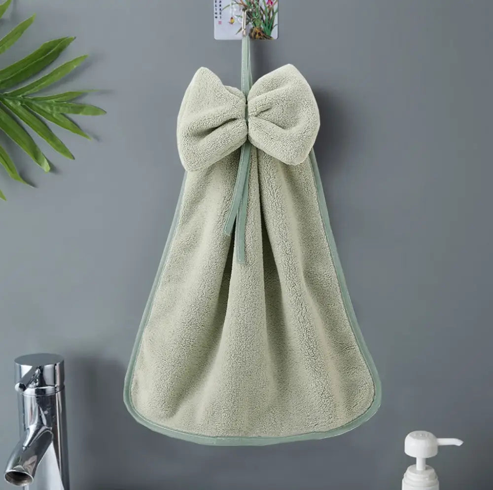 A soft light green bowknot coral velvet hand towel from decorbites hangs neatly on a hook for kitchen cleaning use