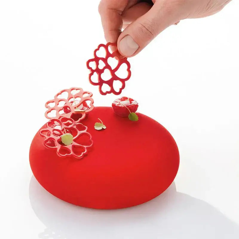 A vibrant red glossy dessert decorated with heart leaf and green leaves made using a gray floral silicone mold set