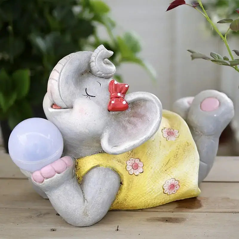 Gray ceramic elephant garden decoration wearing a yellow floral dress holding a blue orb for outdoor use