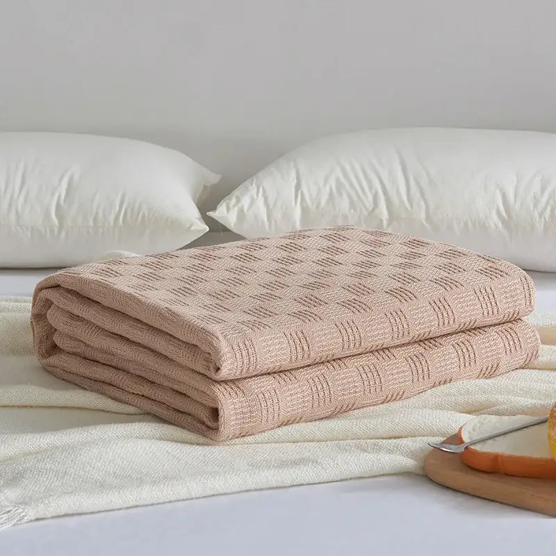 A neatly folded beige knitted cotton waffle towel quilt with a subtle diamond pattern for decorbites bedroom or office