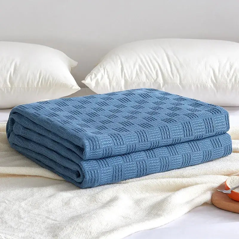 A neatly folded blue woven cotton waffle towel quilt with diamond texture for bedroom or office decorbites cotton waffle