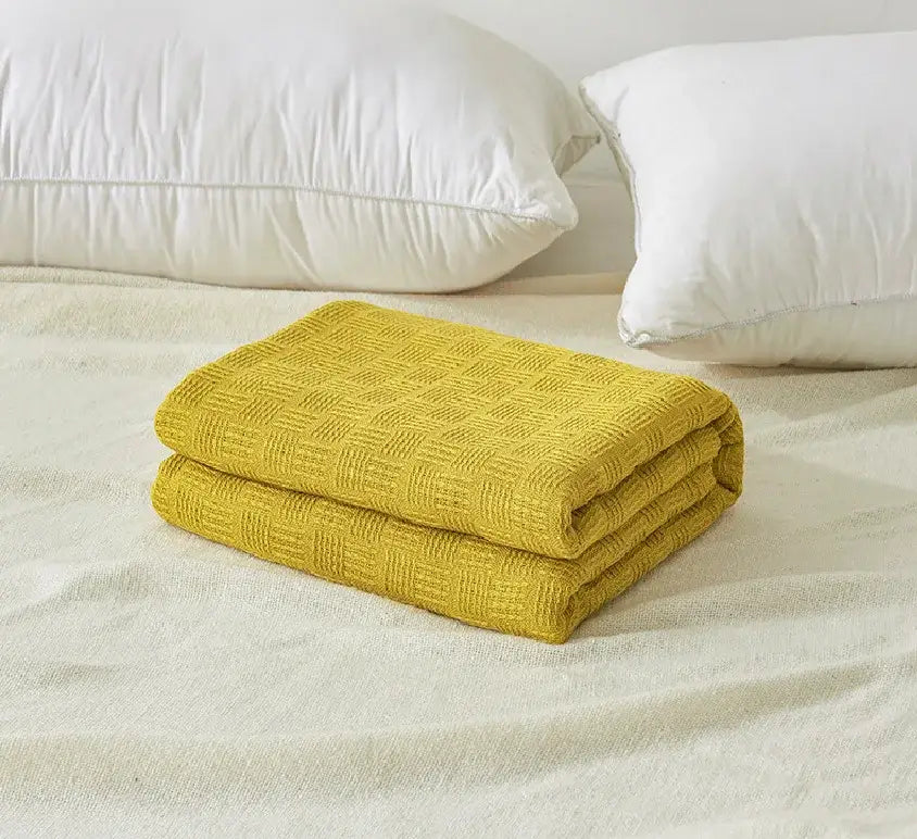 A neatly folded mustard yellow woven cotton waffle towel quilt with diamond texture for bedroom or office decorbites cotton waffle