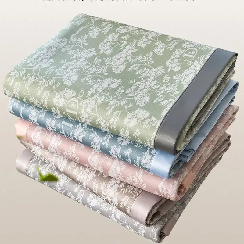 Stacked satin-like bed mat set in soft gray and lavender with delicate white floral patterns and solid-colored borders