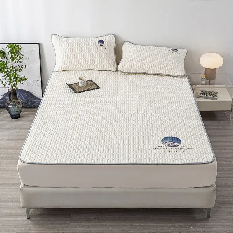 Cream-colored quilted latex bed mat set with textured pattern and blue embroidered logos including matching pillowcases