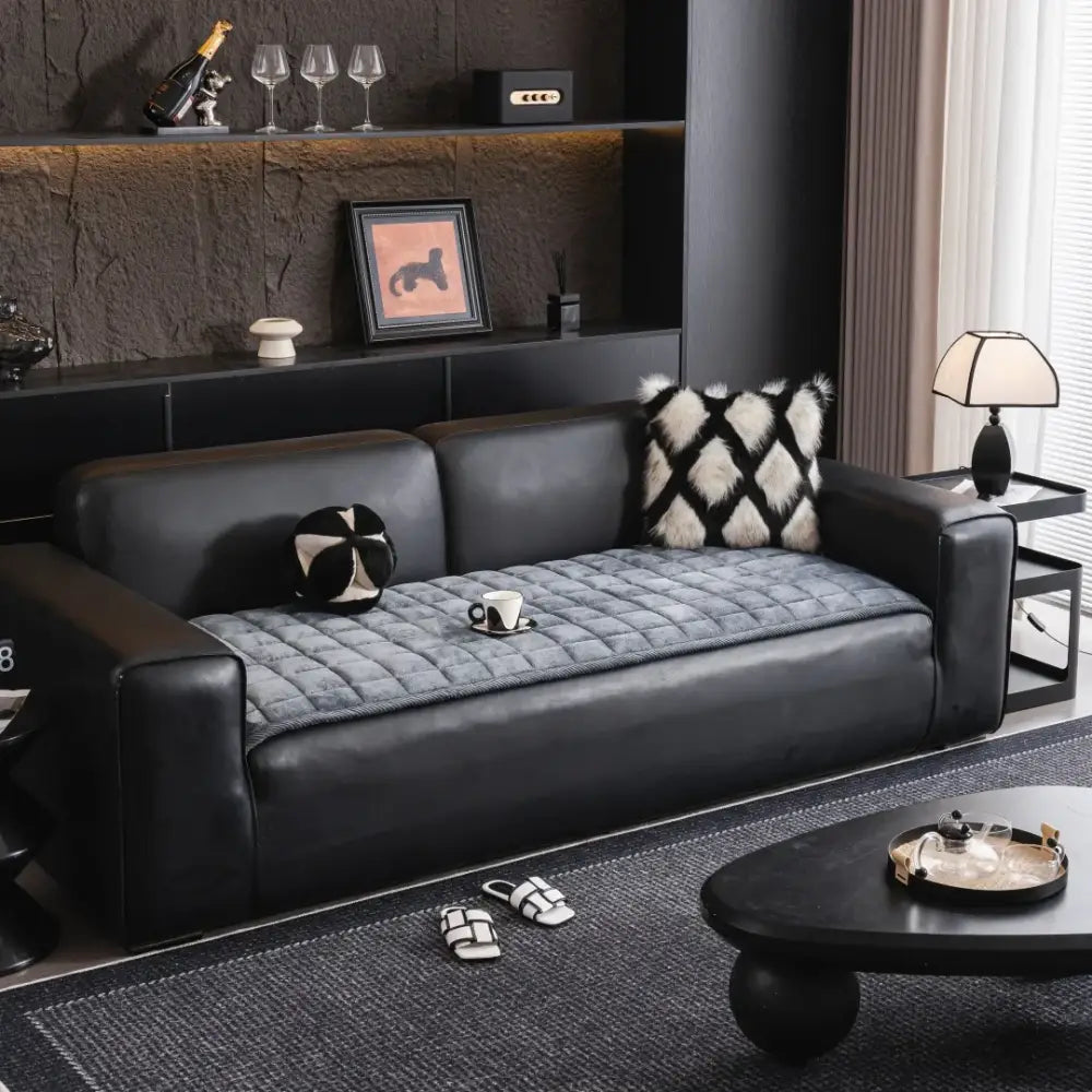Black leather sofa with gray quilted square sofa towel cushion pad and two patterned throw pillows in living room