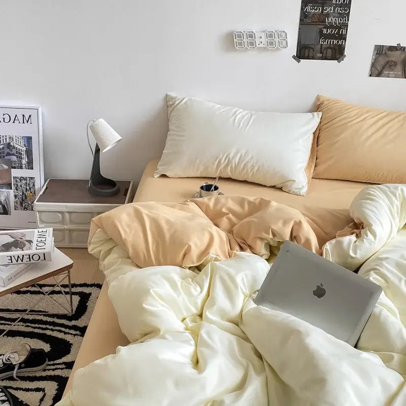 Silver apple macbook laptop resting on cream-colored decorbites cotton quilted duvet cover bed set