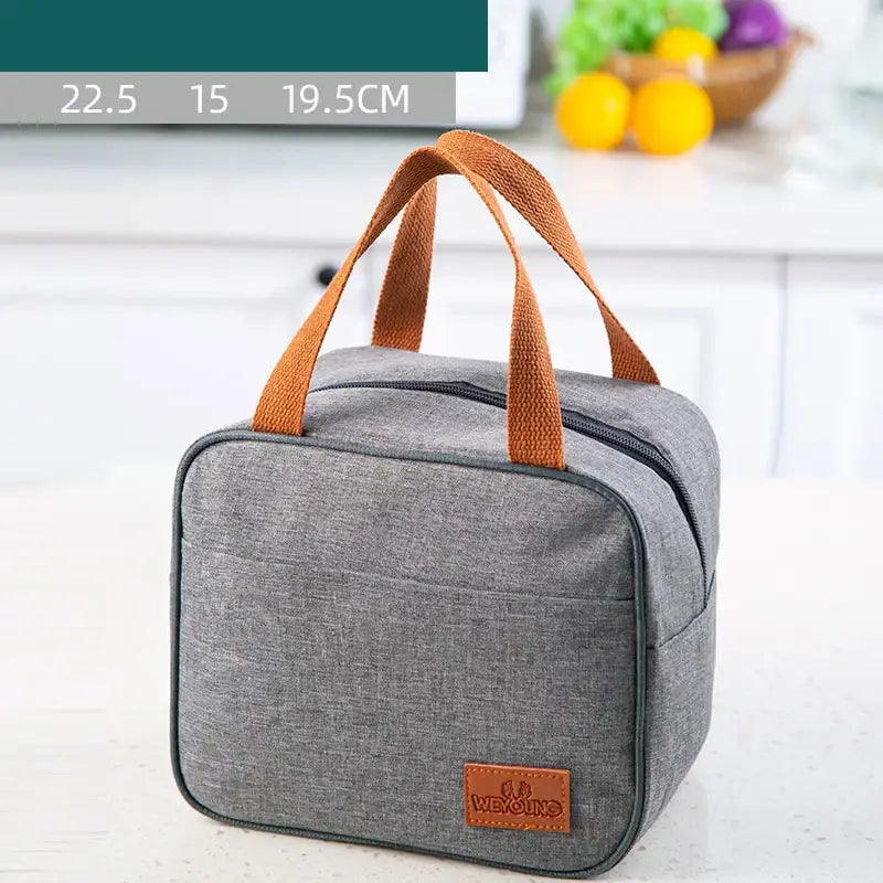 Gray textured insulated lunch bag with brown woven leather handles and matching patch for kitchen thermal use