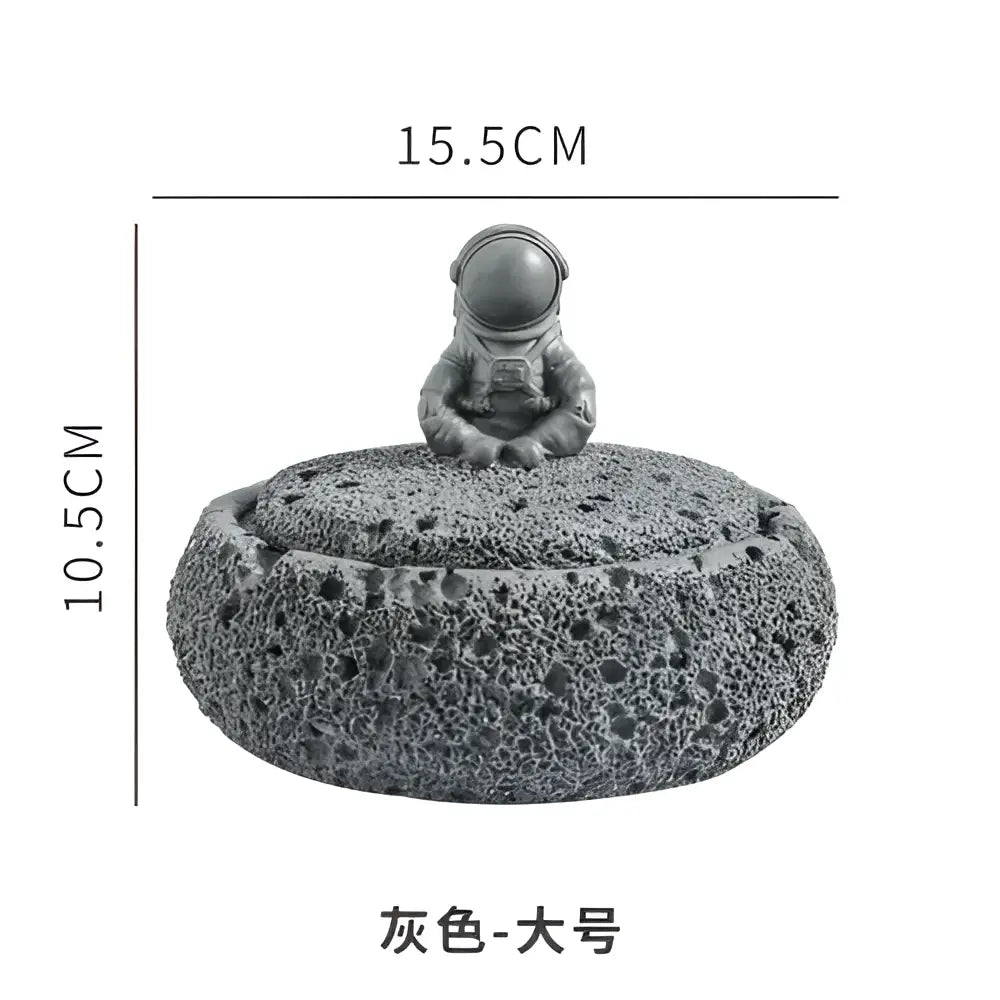 Gray cement astronaut ashtray perched on a textured volcanic stone base for living room decor and use