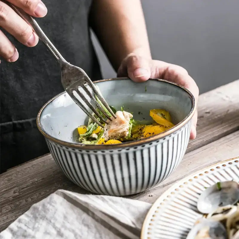 A gray and white striped ceramic bowl with a speckled interior holding salad from decorbites ceramic wedding tableware set