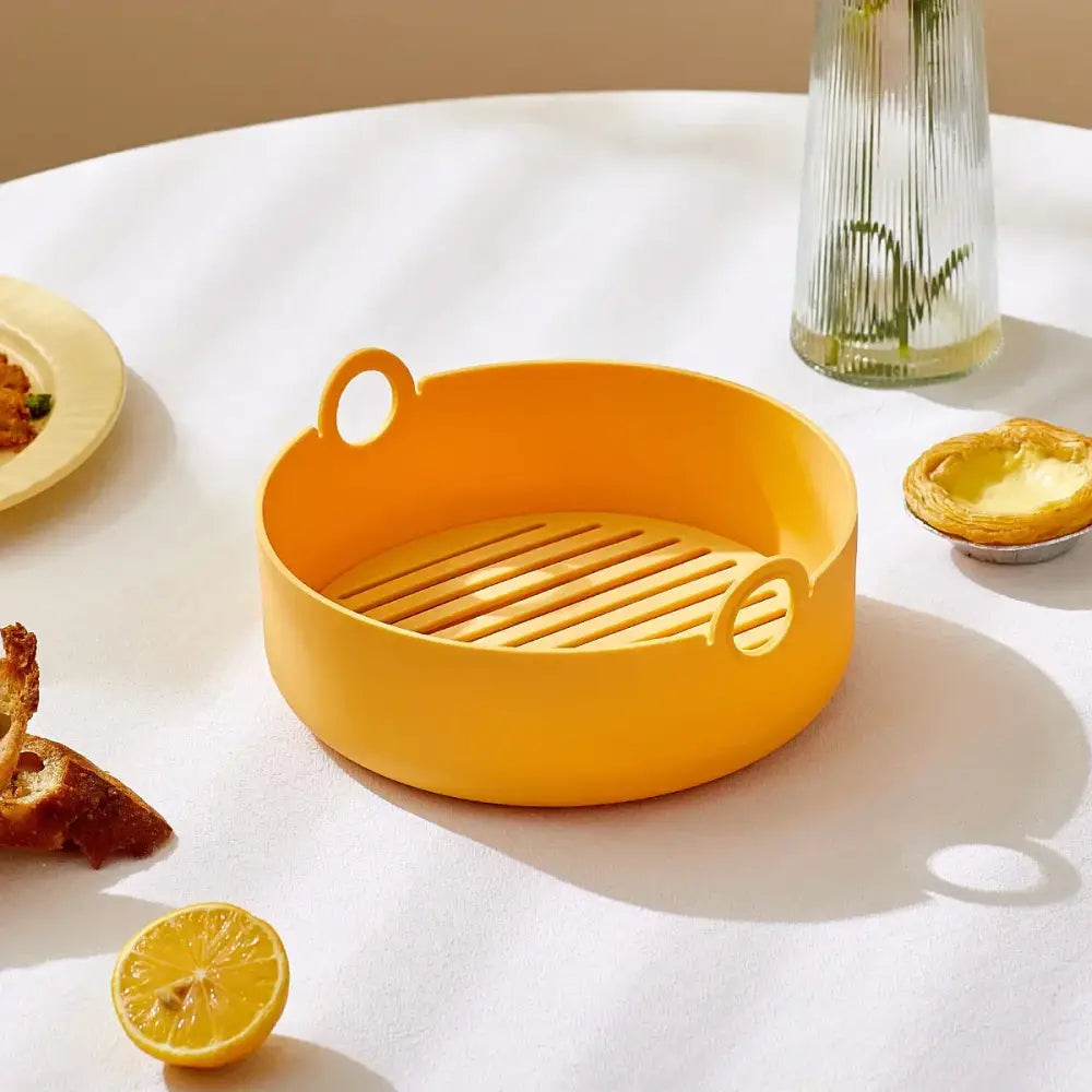 Bright yellow silicone steam basket with looped handles and slatted base for air fryer and baking tray use