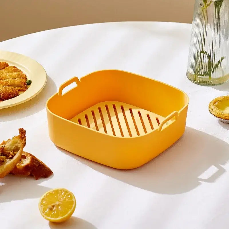 Bright yellow square silicone baking tray with slotted base and handles for air fryer and silicone pot use