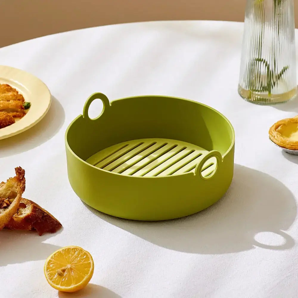Green and black silicone air fryer pot with a lime green silicone steamer basket featuring slatted base and handles