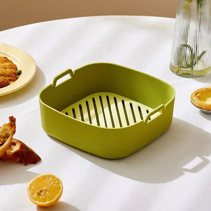 A lime green silicone air fryer baking tray with slatted bottom and side handles for kitchen use