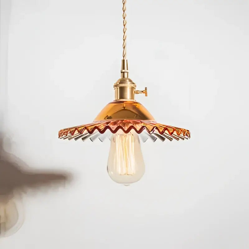 A brass pendant light with scalloped shade and exposed Edison bulb featured in decorbites copper base glass design