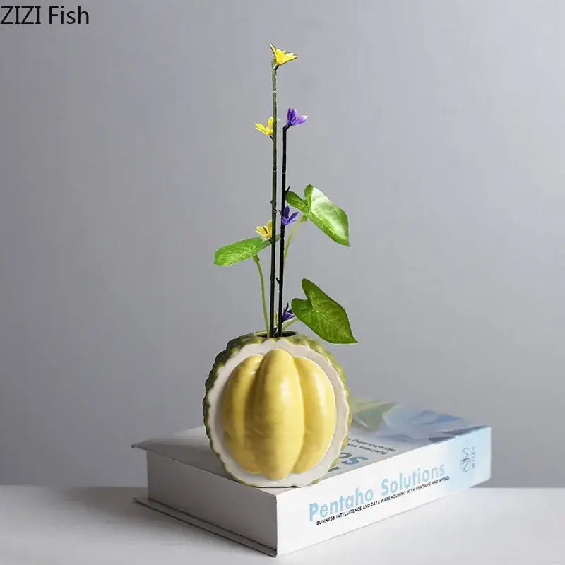 Green and yellow durian ceramic vase shaped like a pumpkin holding purple and yellow flowers for table decor