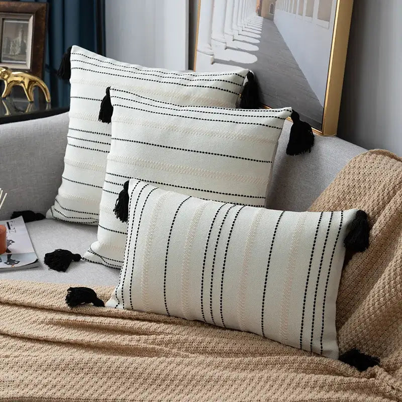 Cream-colored throw pillows with black stripe crochet detailing and tassels complement green black stripe cushion cover