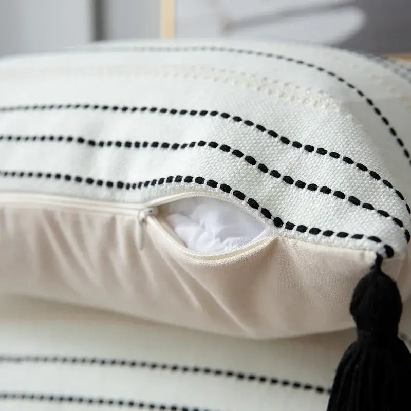 White cushion with black dotted stitching and tassel displayed beside green black stripe crochet cushion cover for living room