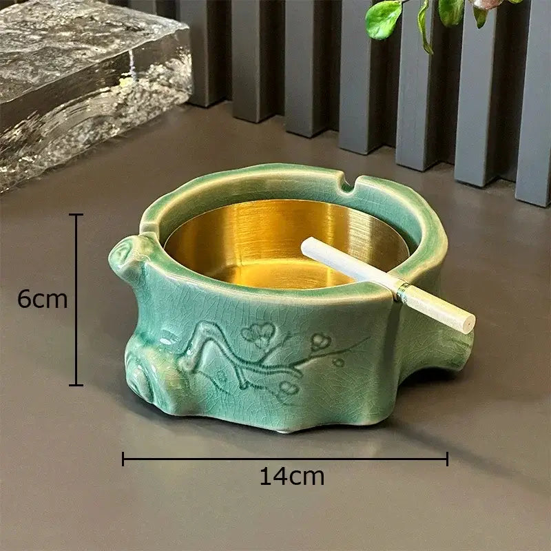Teal ceramic ashtray with gold interior and floral relief alongside green ceramic bamboo tissue box for living room decor