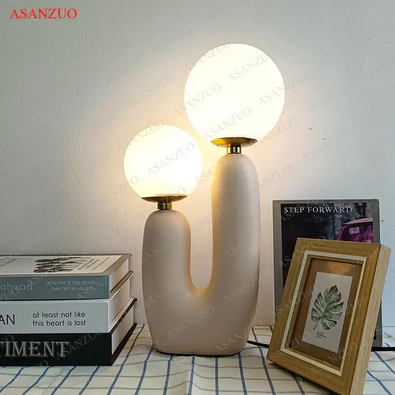 Cream-colored ceramic table lamp with double frosted glass spherical shades and brass accents for bedroom use