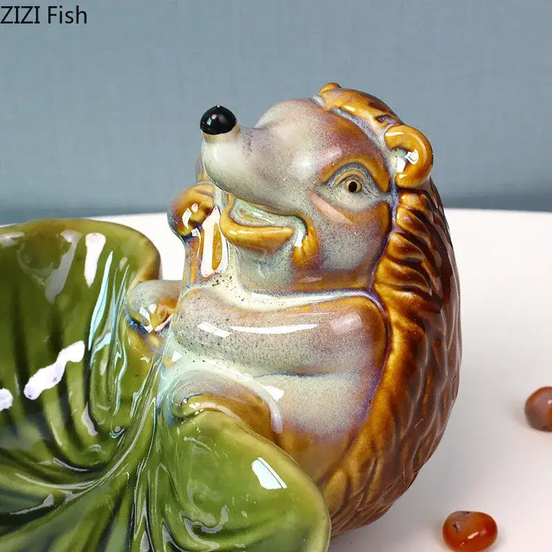 A glossy brown and beige ceramic hedgehog figurine with black bead eyes featured on a decorbites ceramic leaf tray
