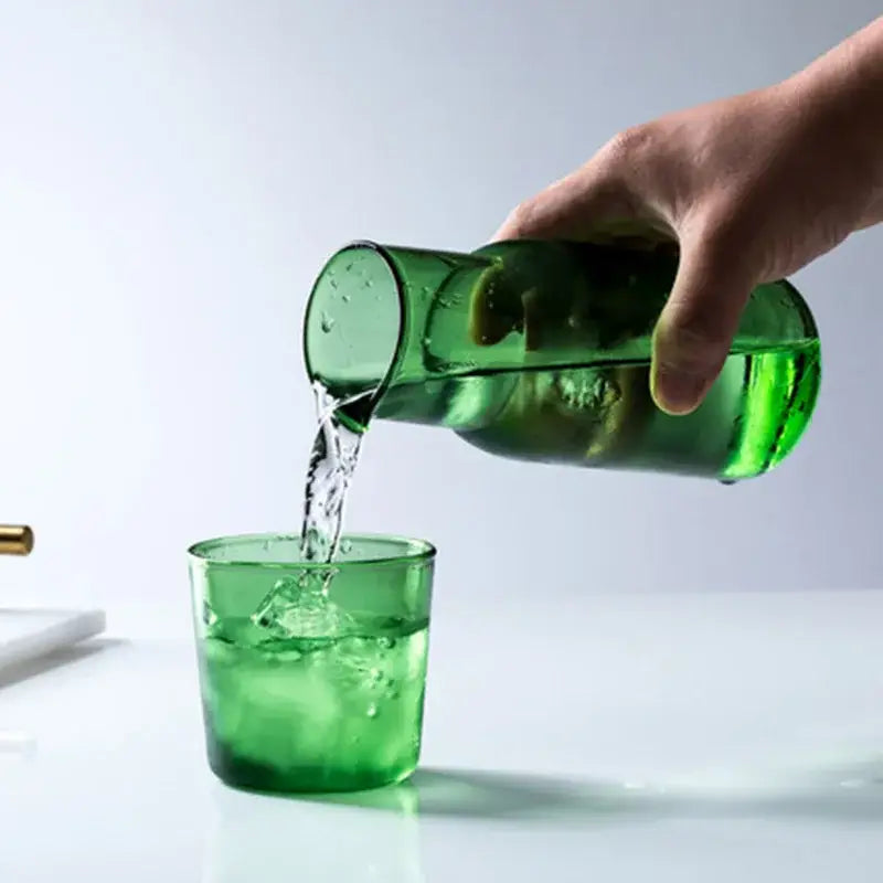 A translucent green glass 550ml bedside water carafe with handle pouring into a matching bedside water tumbler