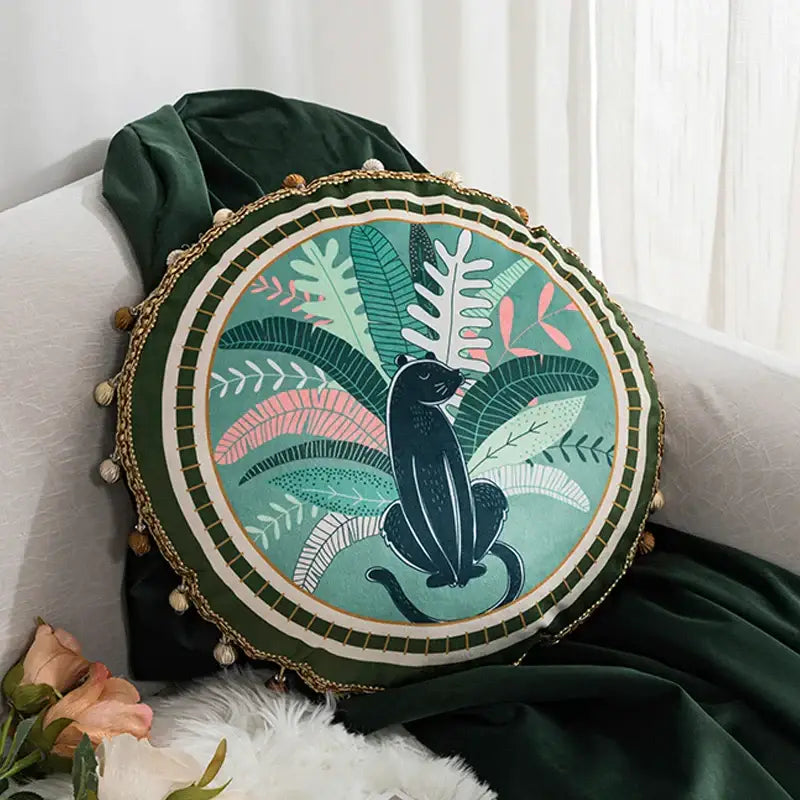 Round cushion cover with black panther and green leaves moss printed on teal velvet framed by dark green velvet and gold pom-poms