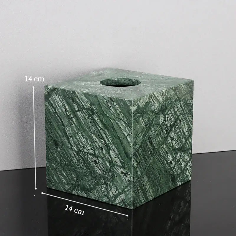 Green marble tissue box with natural stone pattern and circular opening in a marble bathroom set with gold accents