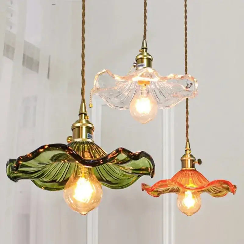 Three hanging glass pendant lights with polished copper fixtures and green and orange leaf-shaped shades for dining room