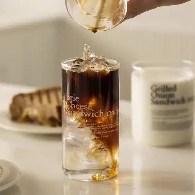 A clear glass coffee cup from decorbites glass coffee set filled with iced coffee featuring a brie cheese sandwich recipe