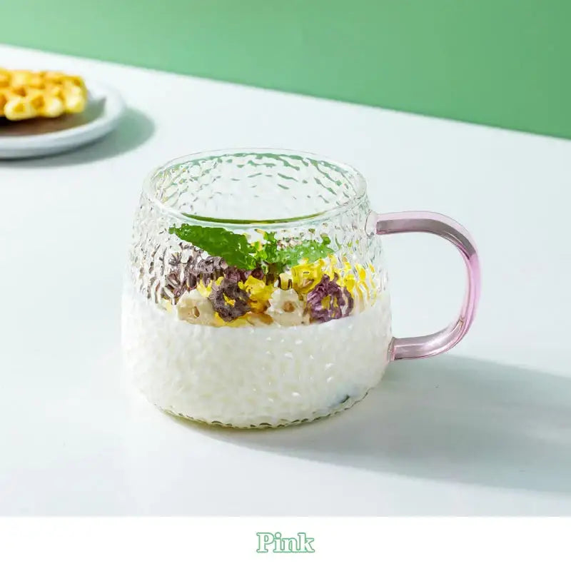 A 400ml hammer pattern glass mug with pink handle filled with layered rice and colorful toppings
