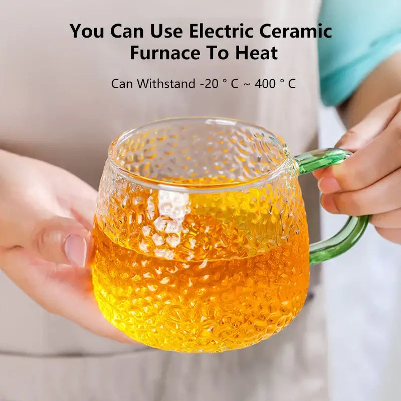 Clear glass mug with 400ml hammer pattern textured surface and green handle filled with golden liquid kitchen glassware