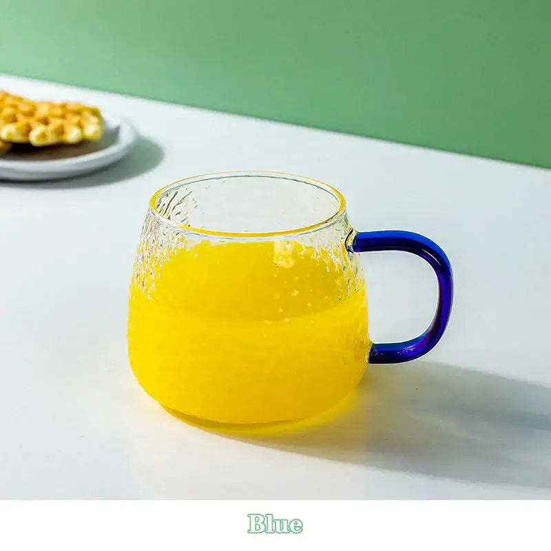 Clear glass mug with hammer pattern texture and vibrant blue handle filled with golden-yellow liquid 400ml hammer pattern