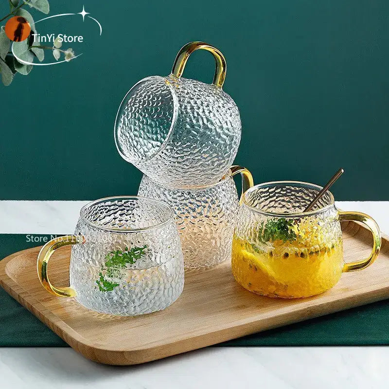 Hammered clear glass water cup with gold handle filled with passionfruit drink and garnished with mint leaves