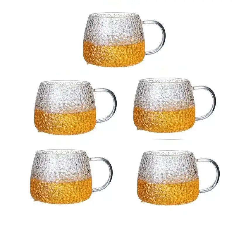 Set of five hammered clear glass water cups with amber lower halves and gold handles for kitchen use