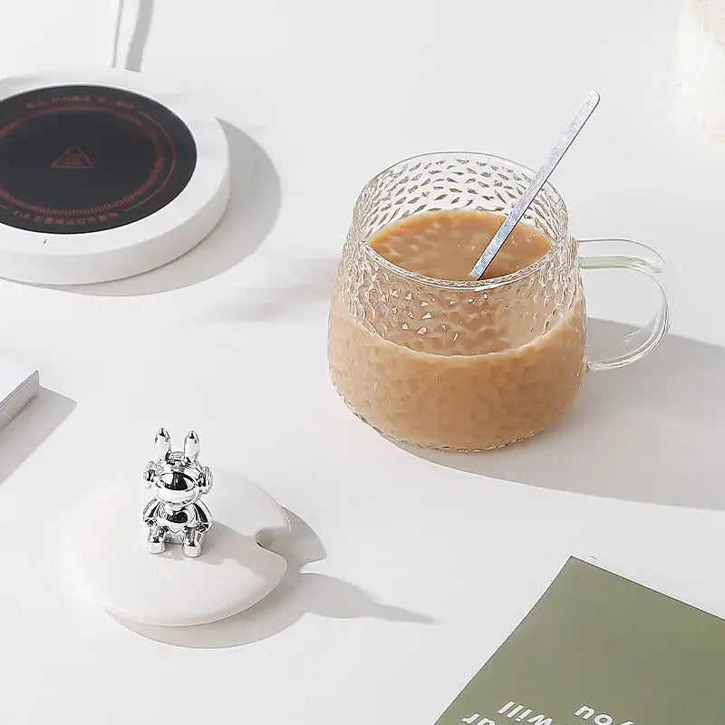 Silver bunny-shaped coaster holder beside hammered clear glass water cup with gold handle for elegant water cup use