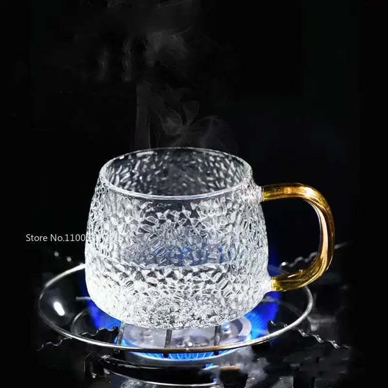 Hammered clear glass water cup with gold handle and textured pattern on matching saucer over a lit burner