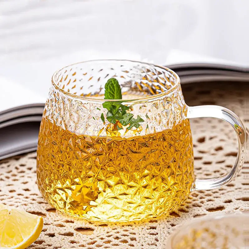 Hammered clear glass water cup with textured diamond pattern and gold handle filled with golden tea and fresh mint leaves