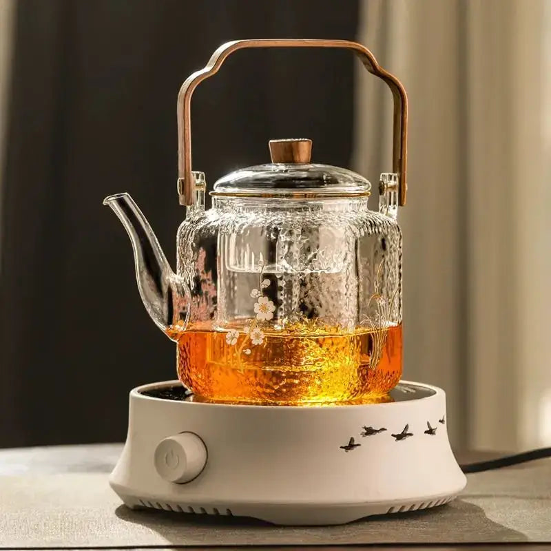 Clear glass teapot with hammered floral etchings and bronze handle filled with amber tea by decorbites glass teapot