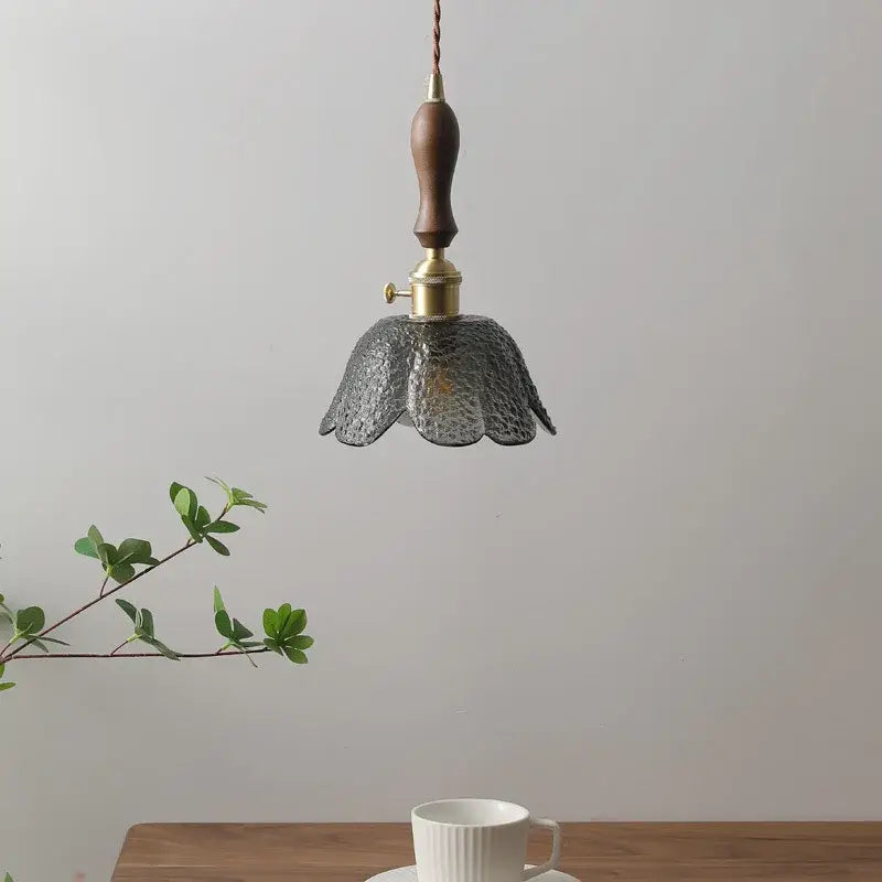 A delicate hammered gray glass led pendant lamp with textured petals, polished brass fixture, and wooden handle for living room lighting