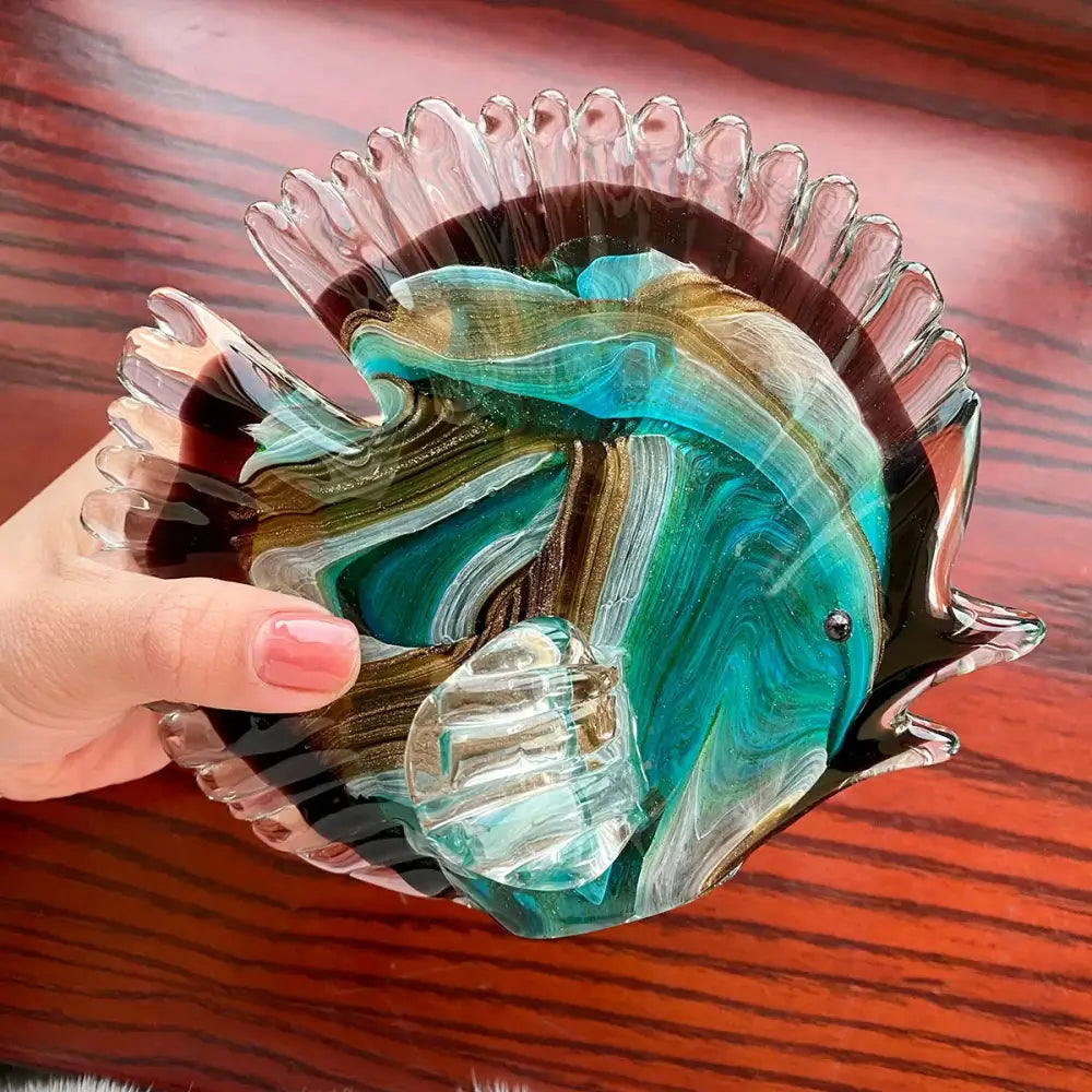 A hand blown tropical glass figurine of a fish with swirling teal green and gold hues for living room decor