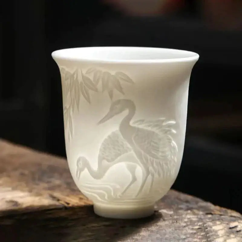 A delicate white porcelain tea cup with hand carved crane and bamboo designs in a translucent white jade tea cup set