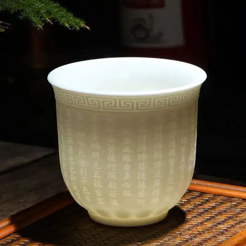 Hand carved translucent white jade tea cup set featuring a celadon ceramic cup with engraved Chinese characters and greek key pattern